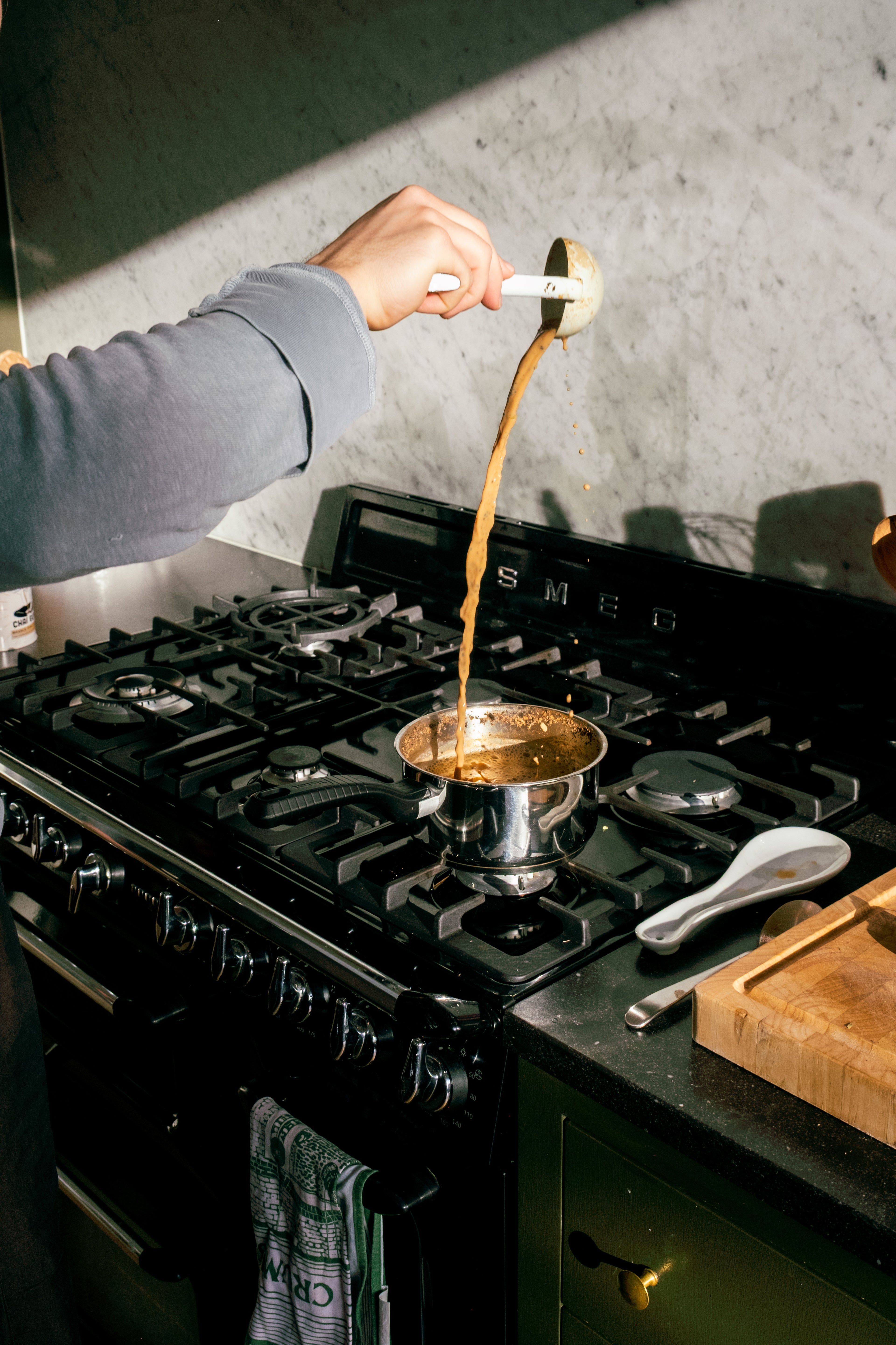 Person pouring a liquid from a spoon into a pot on a stove.
